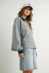 woman wearing a gray striped long sleeve top with navy collar and a cap, paired with denim shorts