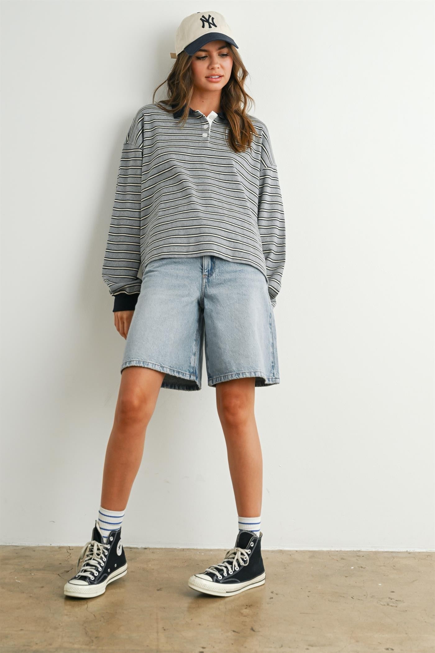 woman wearing a gray and white striped long sleeve polo shirt with denim bermuda shorts and black sneakers