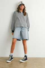 woman wearing a gray and white striped long sleeve polo shirt with denim bermuda shorts and black sneakers