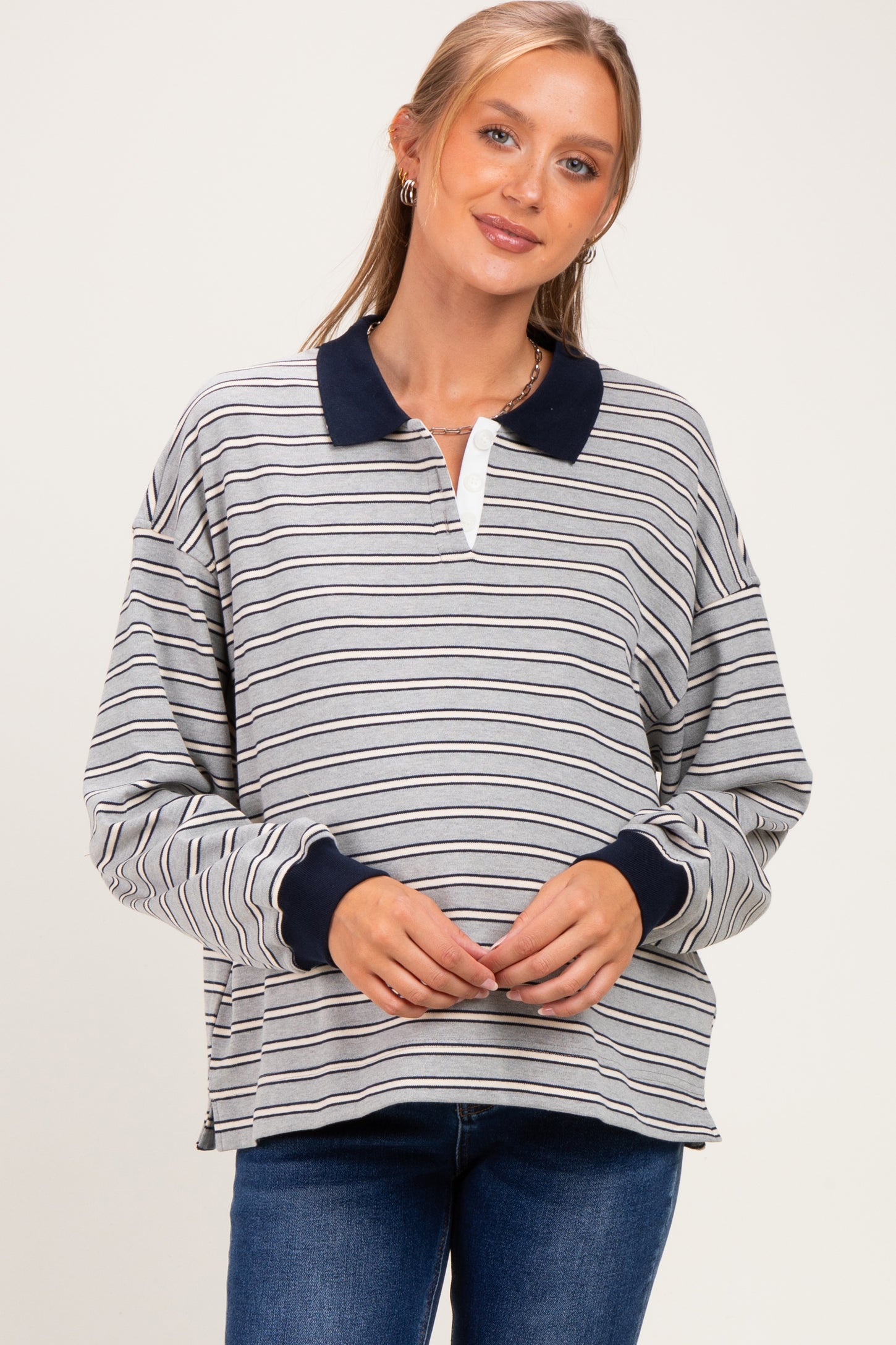 woman wearing a gray and navy striped maternity pullover with a polo collar and long sleeves, showing her baby bump