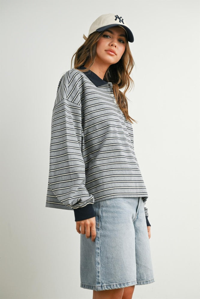 woman wearing a gray striped long sleeve top with navy collar and a cap, paired with denim shorts