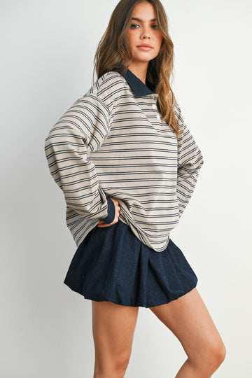 woman wearing a striped oversized sweater with a collared neckline and a navy pleated mini skirt