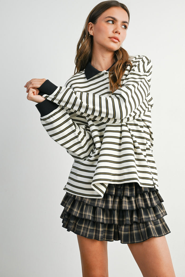 woman wearing a white and black striped oversized long sleeve shirt and a black and tan plaid ruffled mini skirt