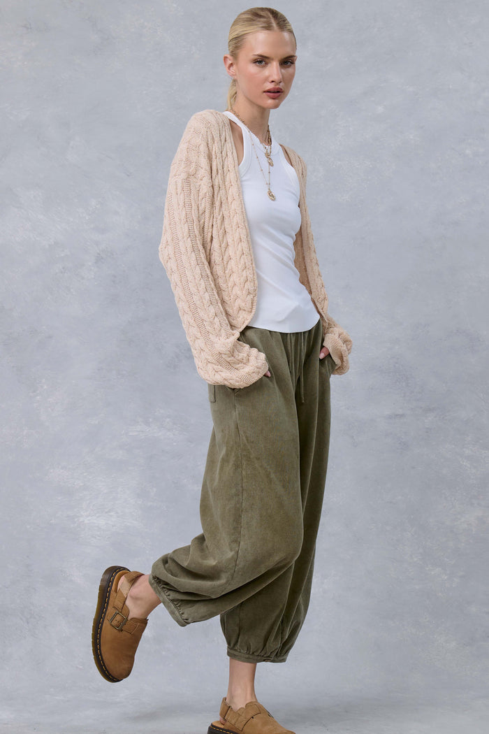 woman wearing a cream cable knit cardigan over a white tank top and olive green baggy pants, paired with tan slip-on shoes