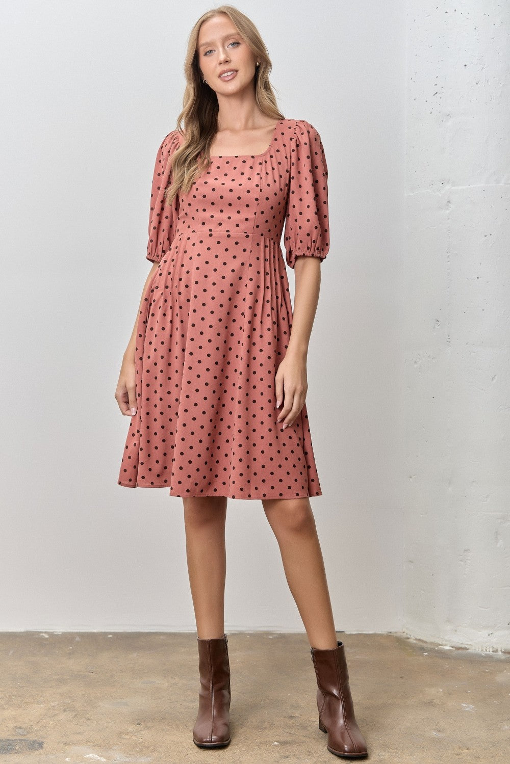 woman wearing a rust-colored dress with puff sleeves and polka dots, standing against a neutral background