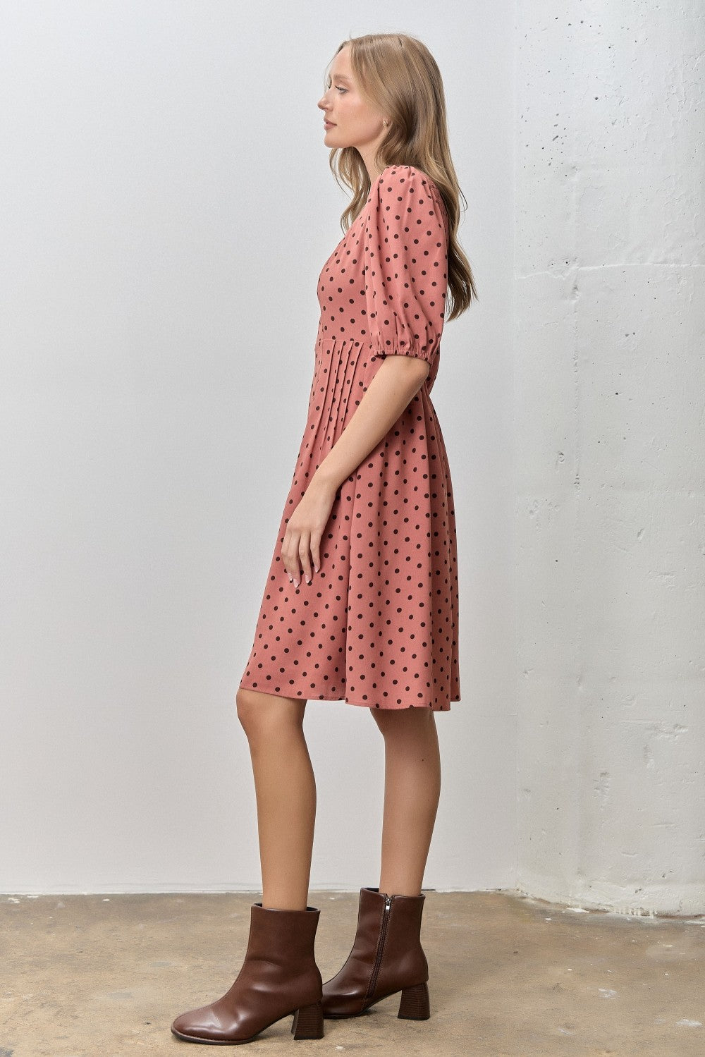 woman wearing a pink polka dot dress with puff sleeves and a flared skirt, paired with brown ankle boots