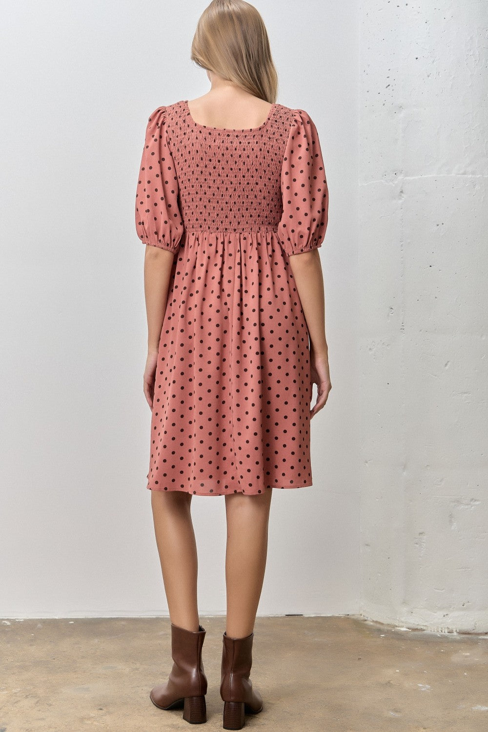 woman wearing a pink smocked dress with puff sleeves and black polka dots, viewed from the back
