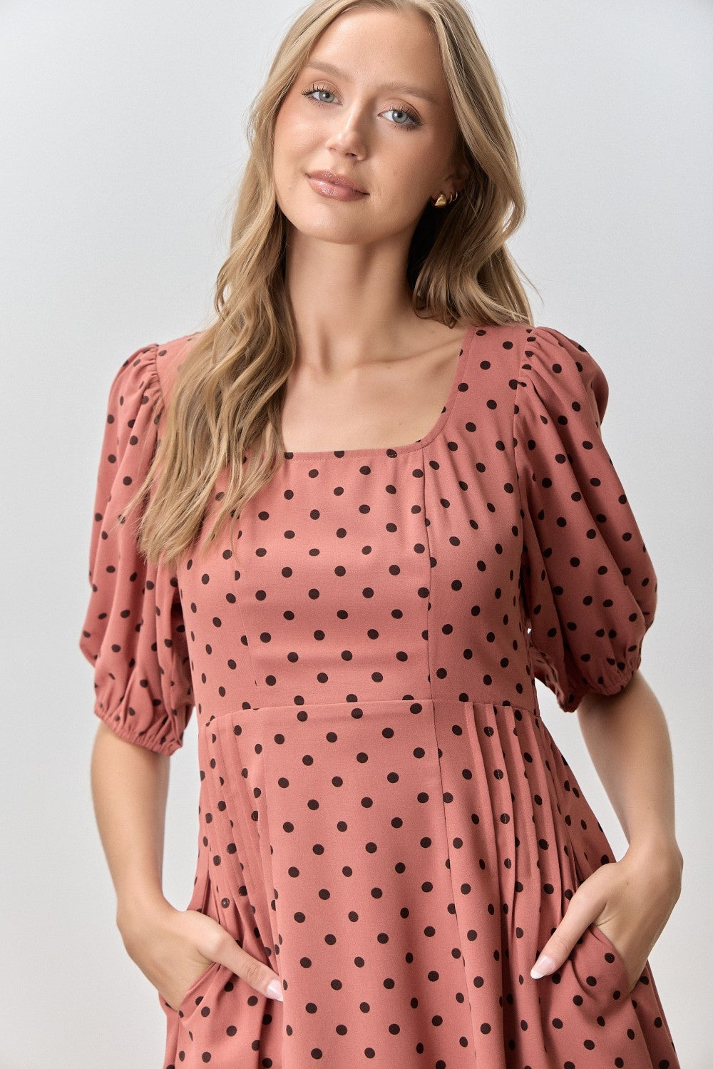 woman wearing a pink polka dot dress with puff sleeves and side pockets