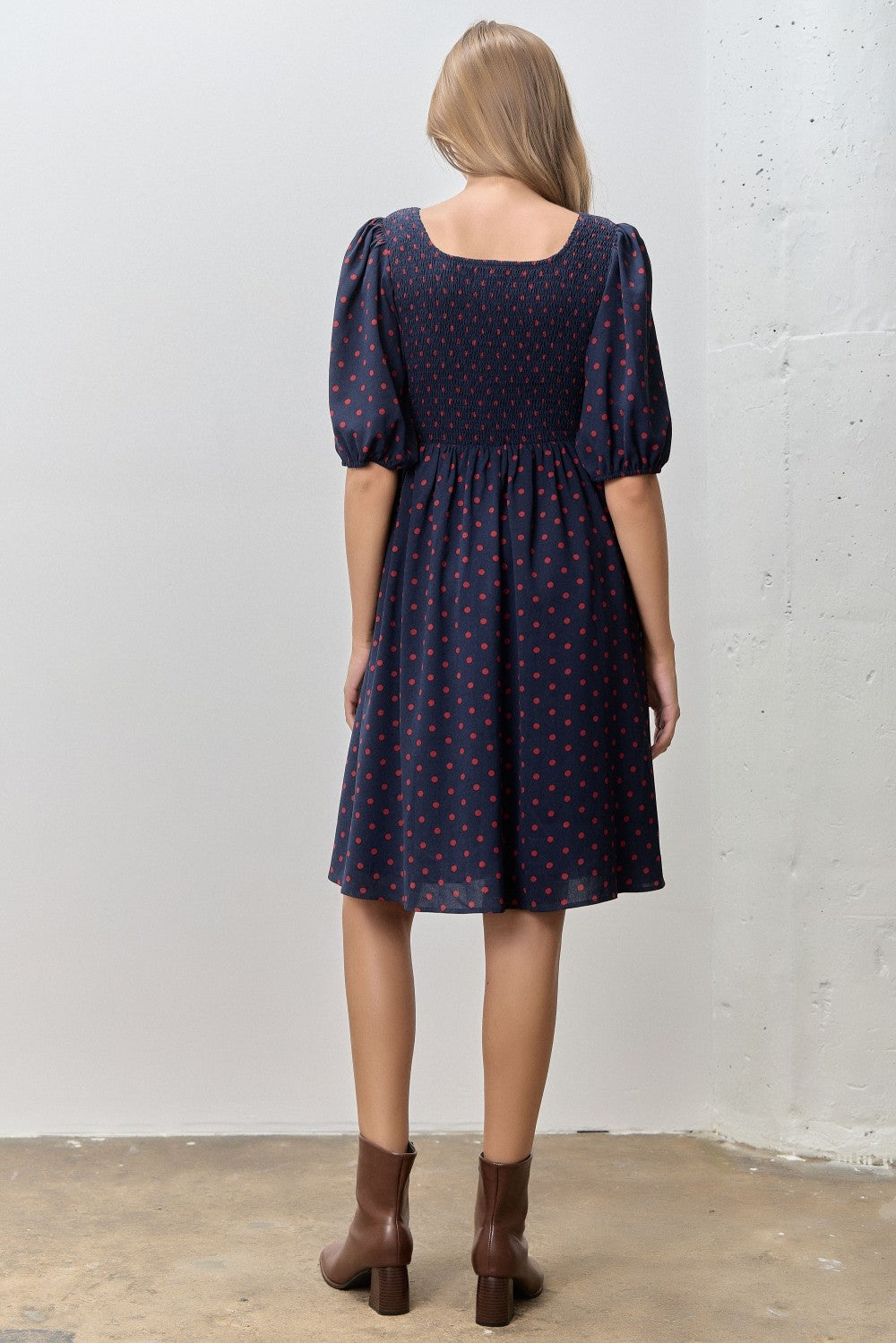 woman wearing a navy blue dress with red polka dots and puff sleeves, shown from the back