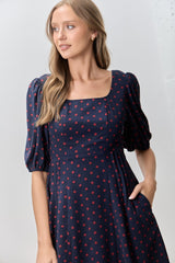woman wearing a navy blue dress with red polka dots and puffed sleeves, featuring a square neckline and pockets