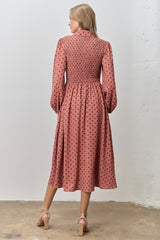 woman wearing a pink polka dot mid-length dress with smocked bodice and long sleeves, viewed from the back