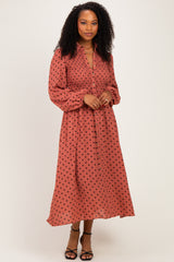 woman wearing a rust-colored long sleeve maxi dress with black polka dots and a smocked bodice, standing with hands on hips