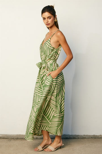 woman wearing a green and cream striped maxi dress with a tie waist and pockets, standing against a light background