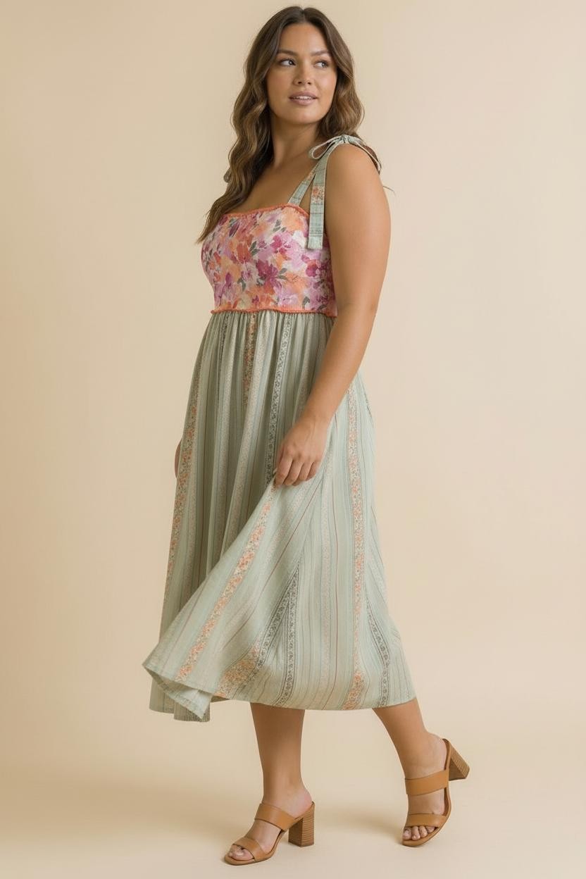 woman wearing a floral print pink and green midi dress with straps and a flowing skirt, paired with tan heeled sandals