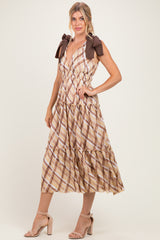 woman wearing a brown and beige plaid midi dress with a tiered skirt and bow tie straps, standing in a neutral background