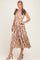 woman wearing a brown and beige plaid midi dress with a tiered skirt and bow tie straps, standing in a neutral background