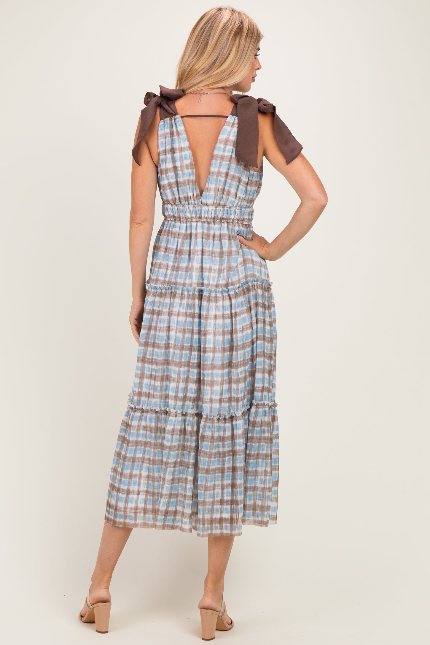 woman wearing a beige and blue checkered midi dress with tied shoulder straps and a tiered skirt, shown from the back