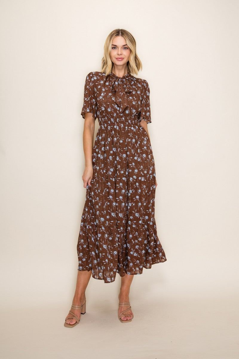 woman wearing a brown floral midi dress with short sleeves and a tie neck detail