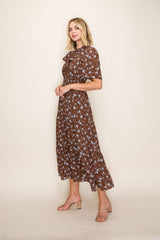 woman wearing a brown floral midi dress with a ruffled neckline and short sleeves, standing against a neutral background
