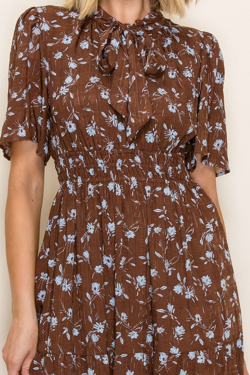 woman wearing a brown floral midi dress with short sleeves and a tie neck detail