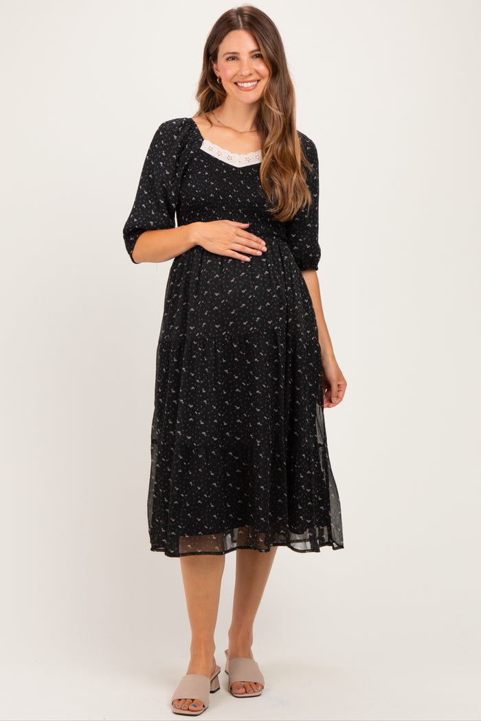 woman wearing a black floral maternity dress with a fitted bodice and flowing skirt, holding her baby bump
