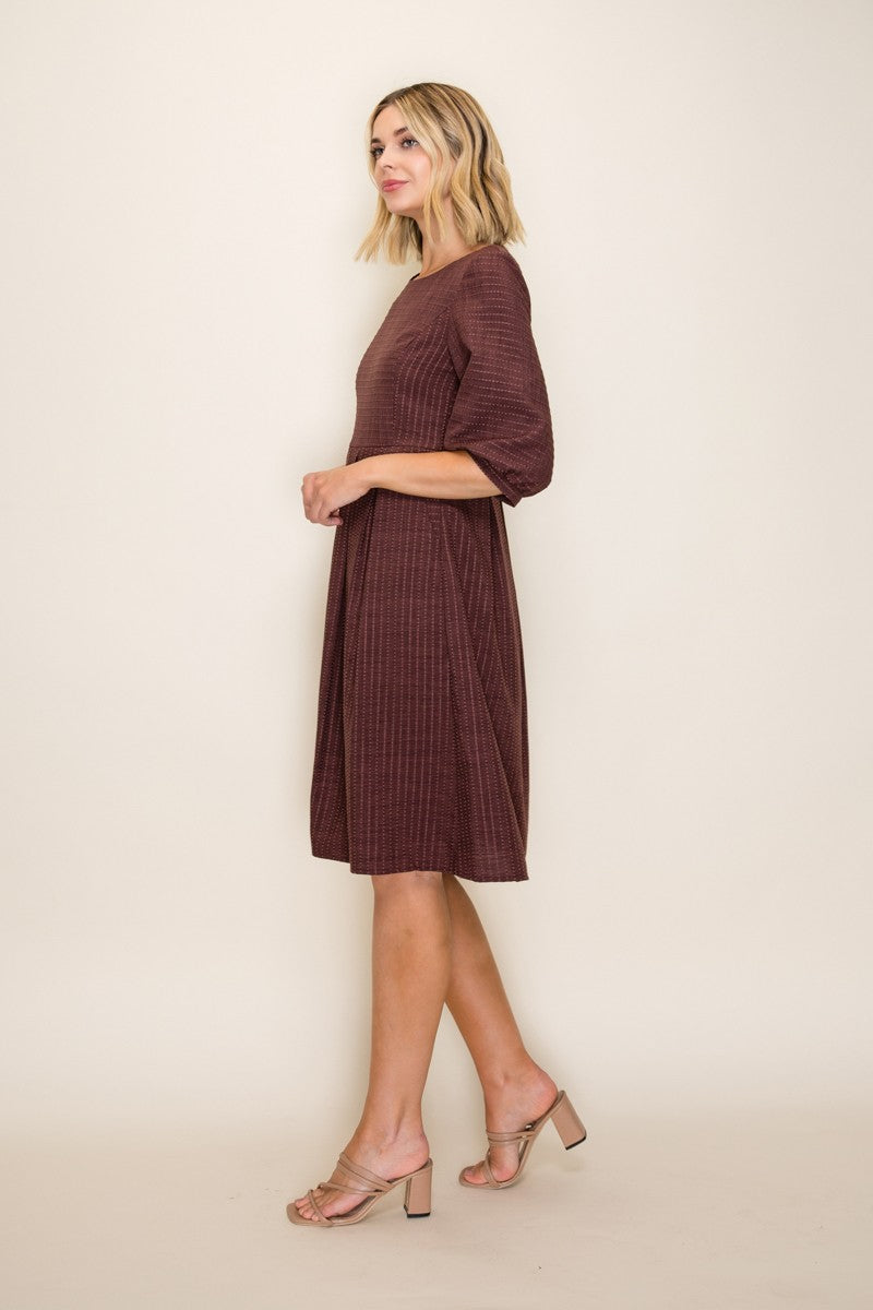 woman wearing a maroon short sleeve dress with a textured pattern and flowing skirt, styled with beige heels
