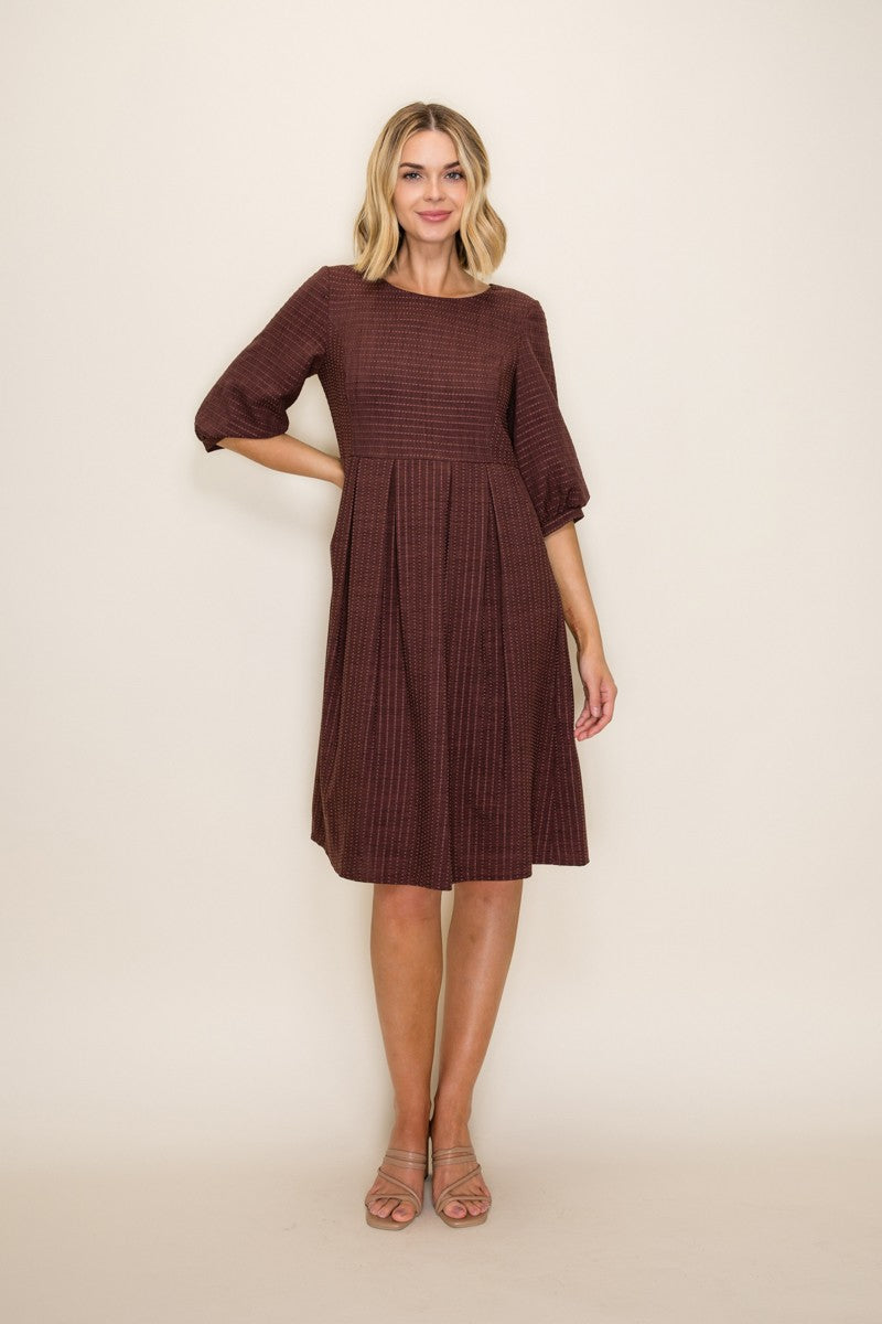 woman wearing a maroon textured above-the-knee dress with three-quarter sleeves and a pleated skirt