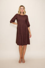 woman wearing a maroon textured above-the-knee dress with three-quarter sleeves and a pleated skirt