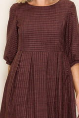 woman wearing a maroon pleated dress with three-quarter sleeves and subtle stripe patterns