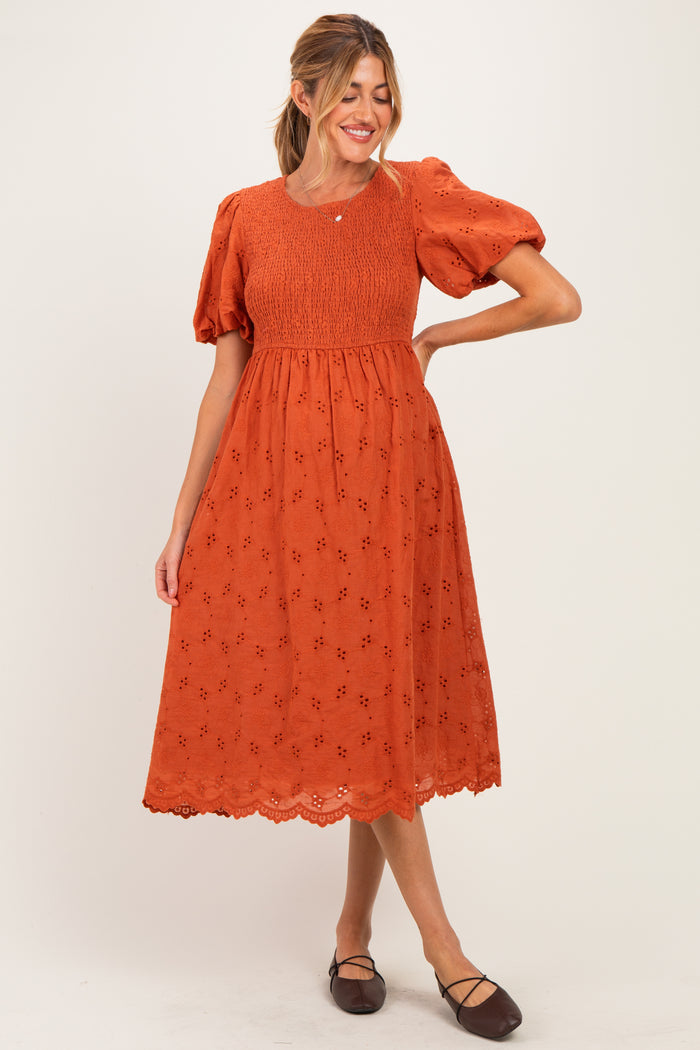 woman wearing an orange maternity dress with puff sleeves and floral embroidery, showing her baby bump