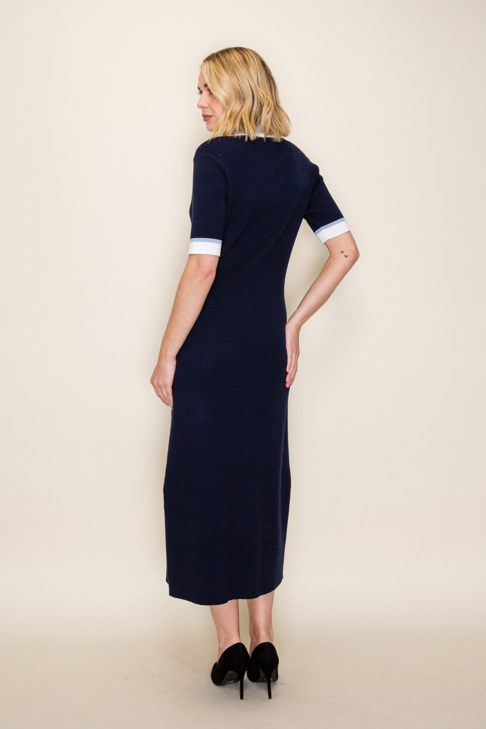 woman wearing a navy blue midi dress with fitted silhouette and white cuff details, shown from the back