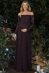 woman wearing a dark purple off-the-shoulder lace maternity dress and holding her baby bump in a garden setting