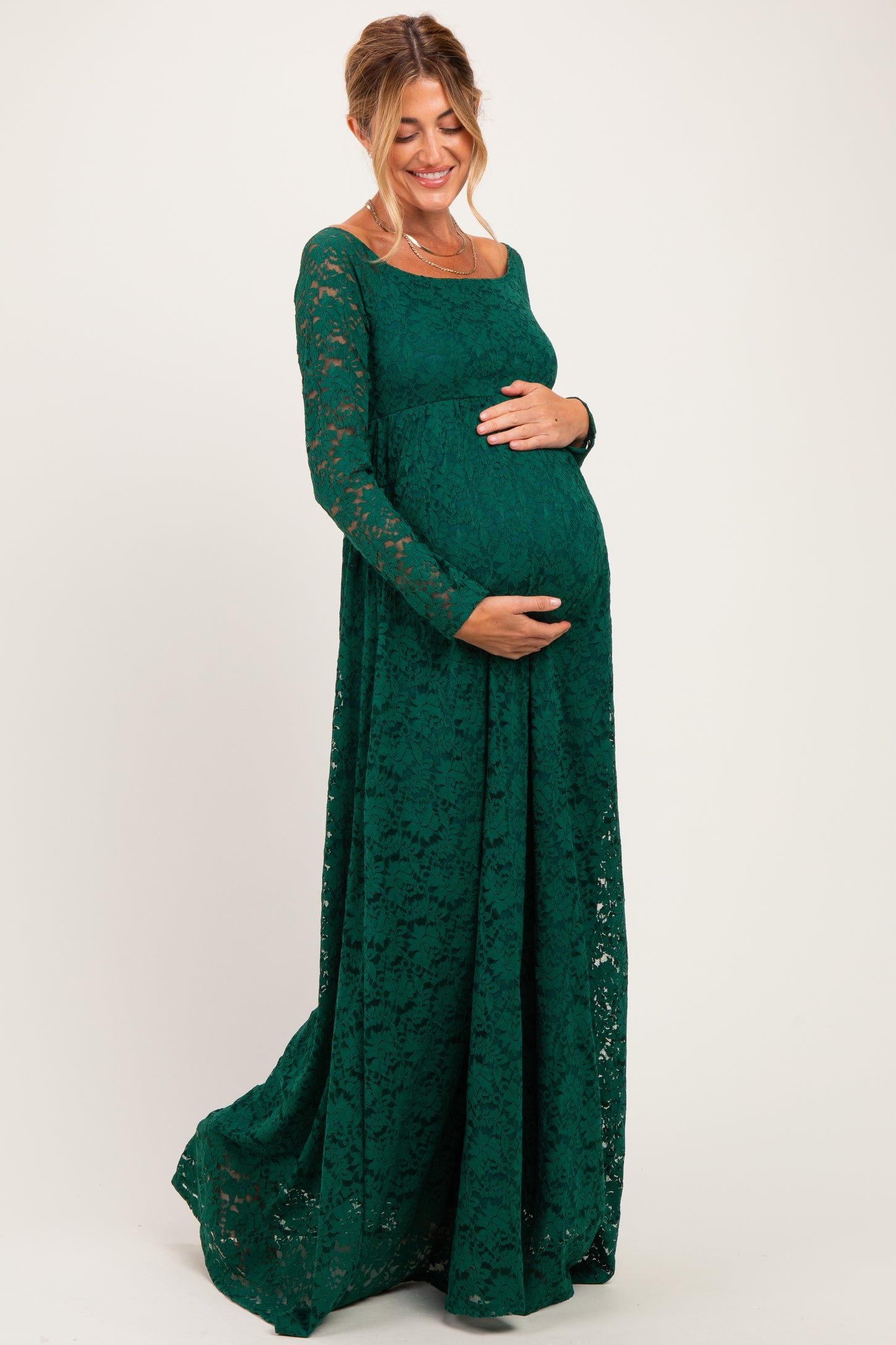 woman wearing a green lace maternity dress and holding her baby bump