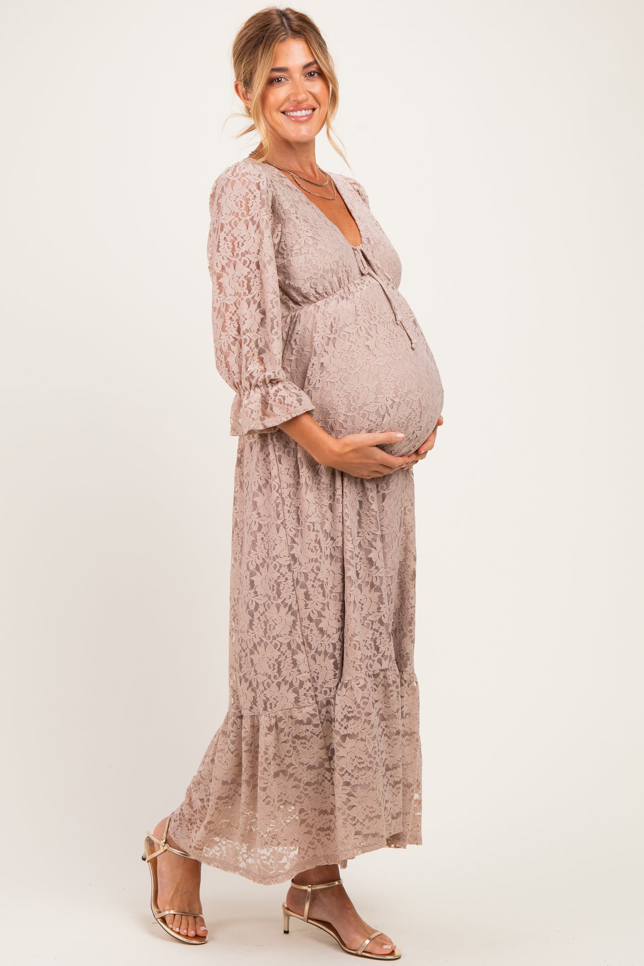 woman wearing a taupe lace maternity maxi dress and holding her baby bump