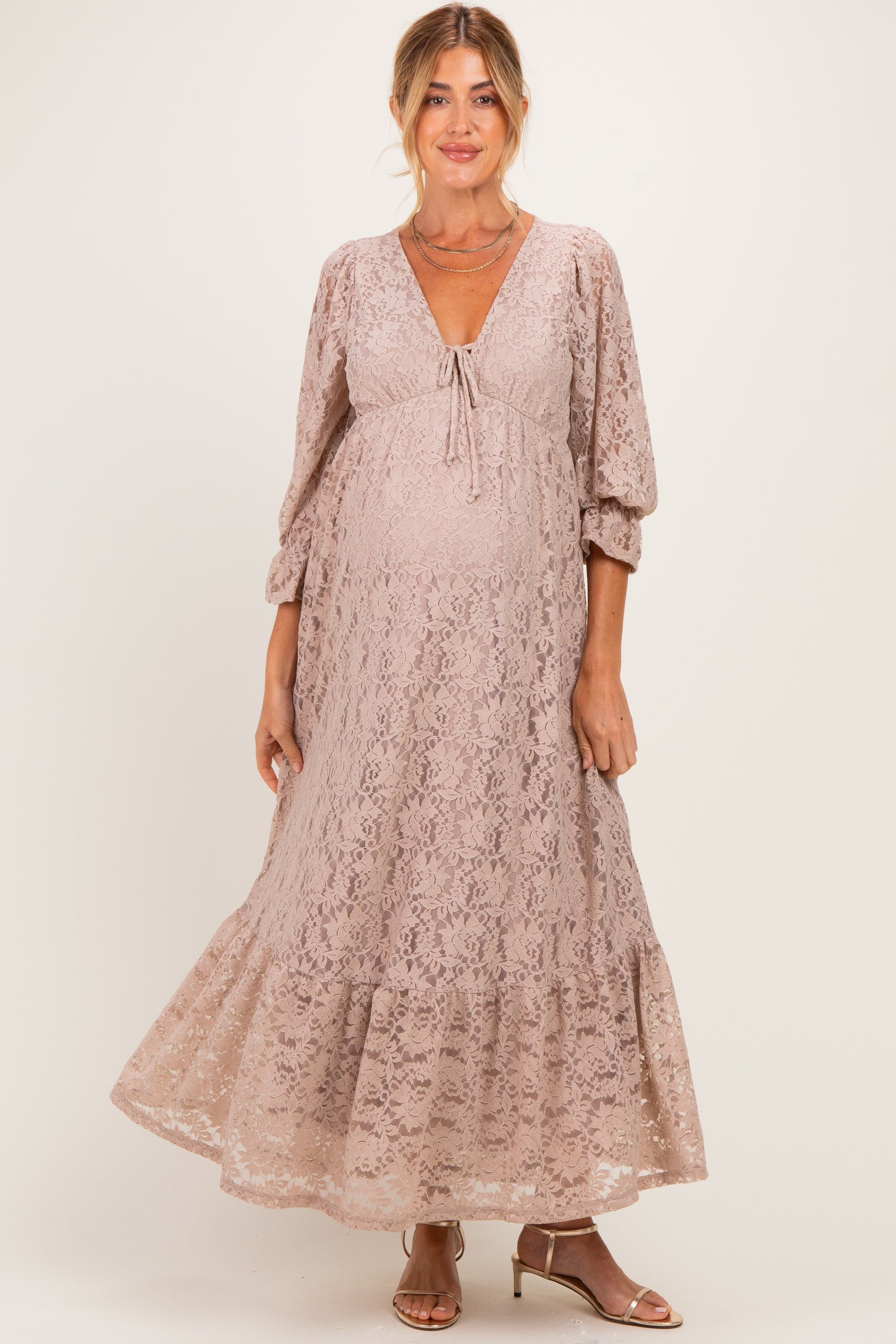woman wearing a light pink lace maternity maxi dress with a tie detail and bell sleeves, showing her baby bump