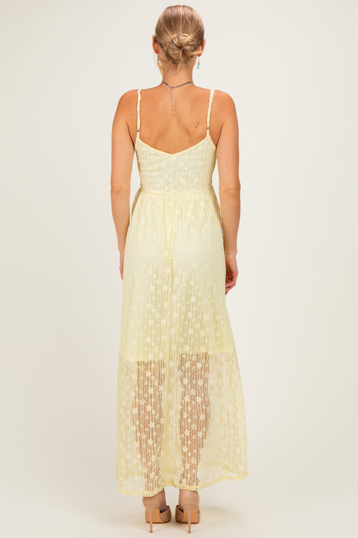 woman wearing a light yellow lace maxi dress with a fitted bodice and a flowing skirt, shown from the back