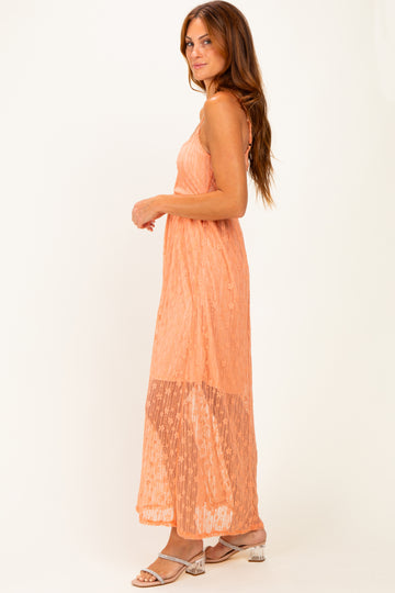 woman wearing an orange lace maxi dress with a fitted bodice and flowing skirt, standing in profile
