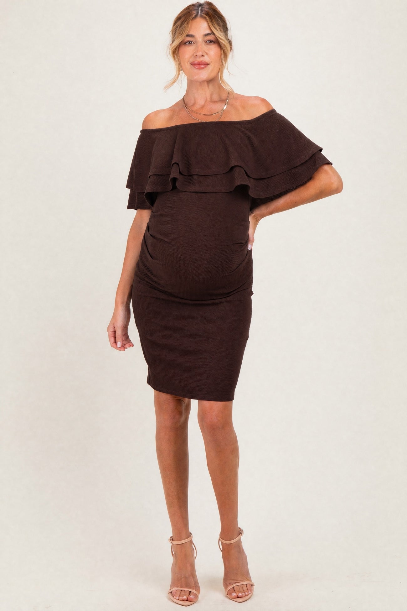 woman wearing a chocolate brown off-the-shoulder maternity dress with ruffle details and a visible baby bump