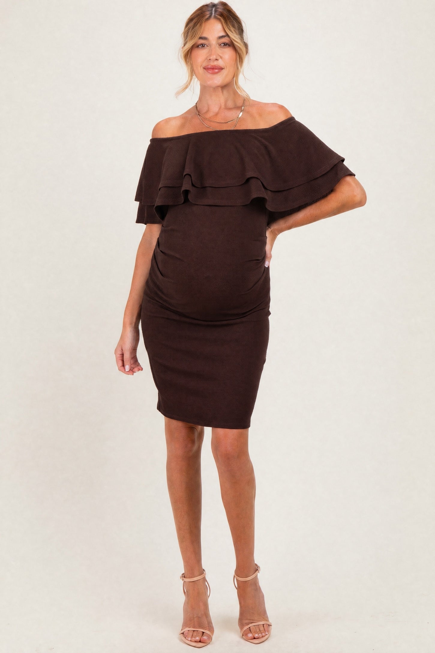 woman wearing a chocolate brown off-the-shoulder maternity dress with ruffle details and a visible baby bump