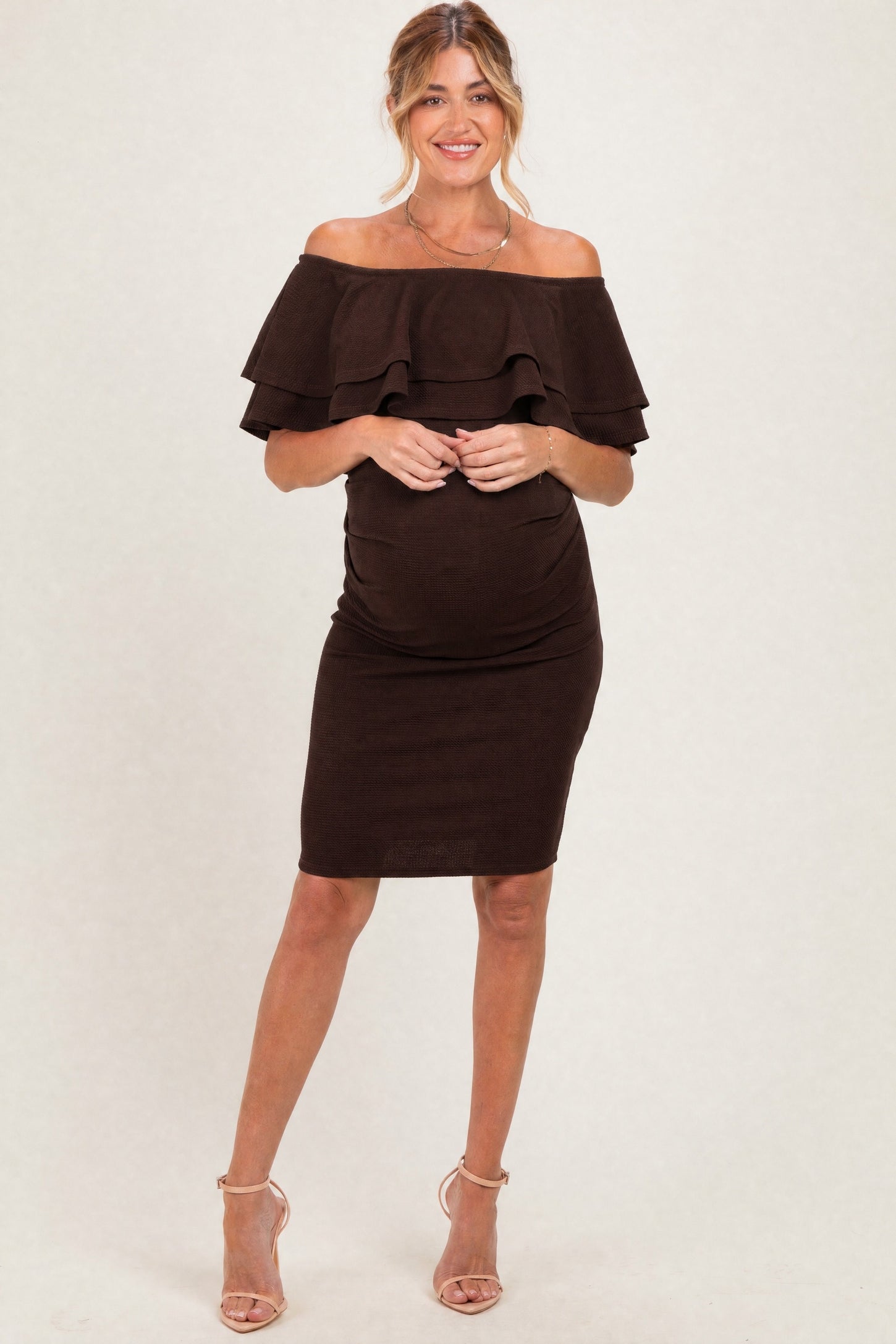 woman wearing a brown off-the-shoulder maternity dress with ruffles and a visible baby bump