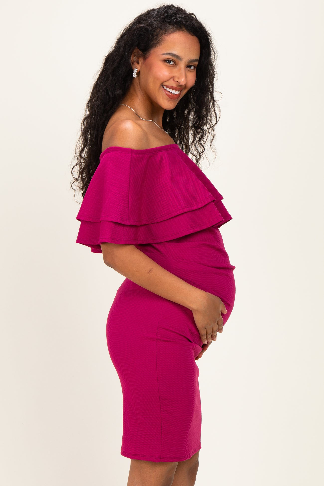 woman wearing a hot pink off-the-shoulder maternity dress with layered ruffles and holding her baby bump