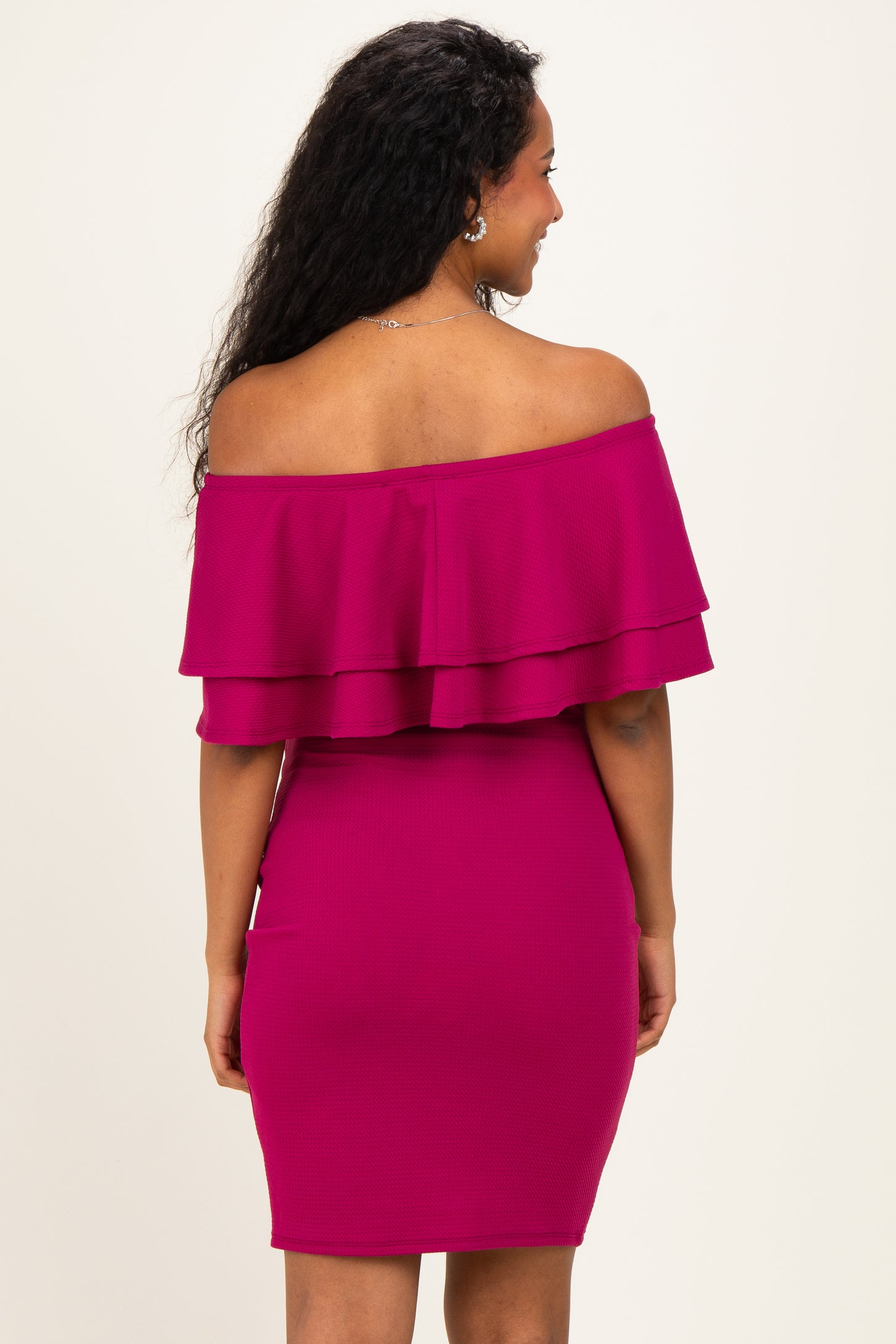 woman wearing a vibrant pink off-the-shoulder maternity dress with layered ruffles and a fitted silhouette