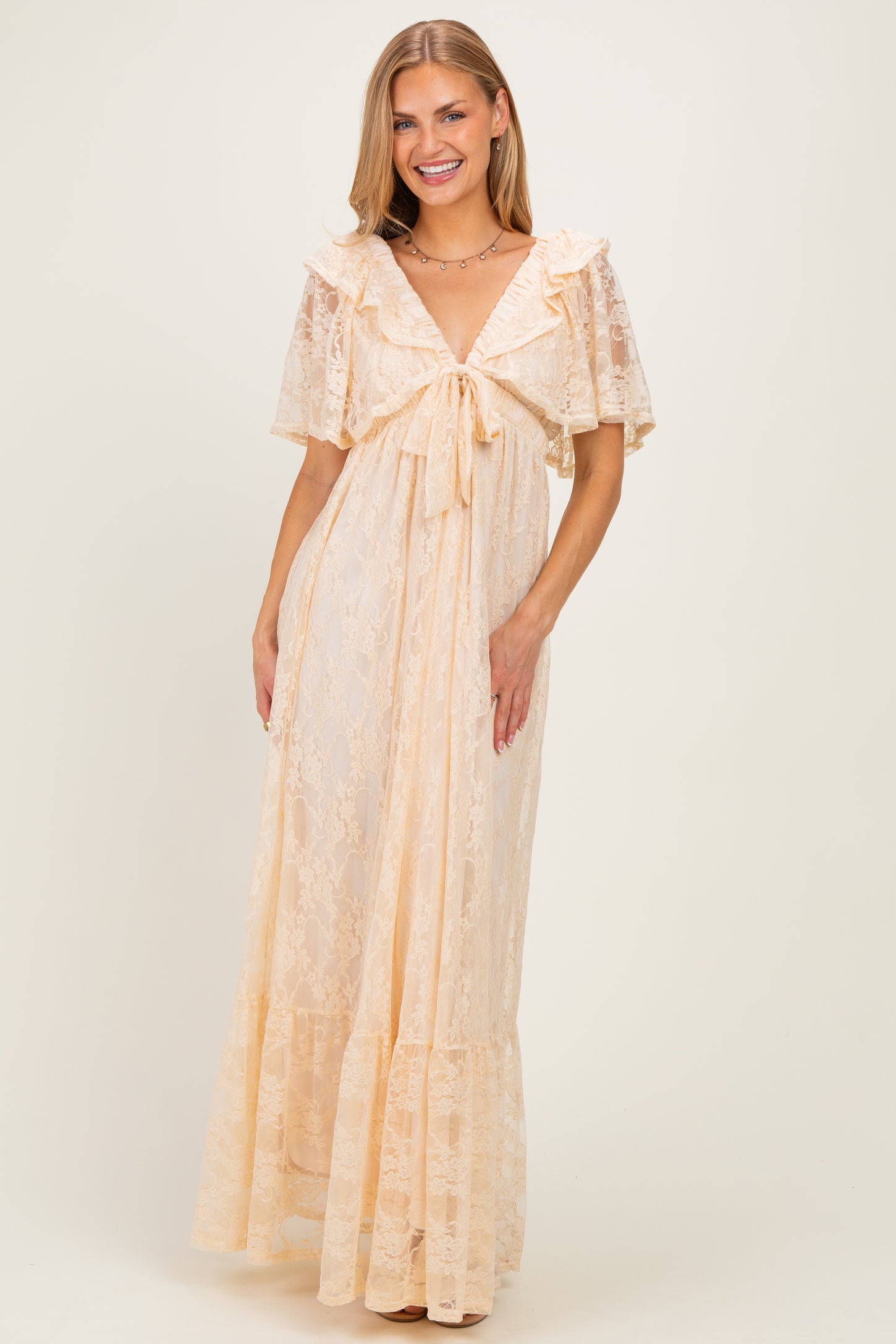 woman wearing a light peach lace maxi dress with a tie front and ruffled sleeves