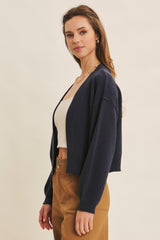 woman wearing a navy blue cropped cardigan over a white tank top and tan high-waisted pants