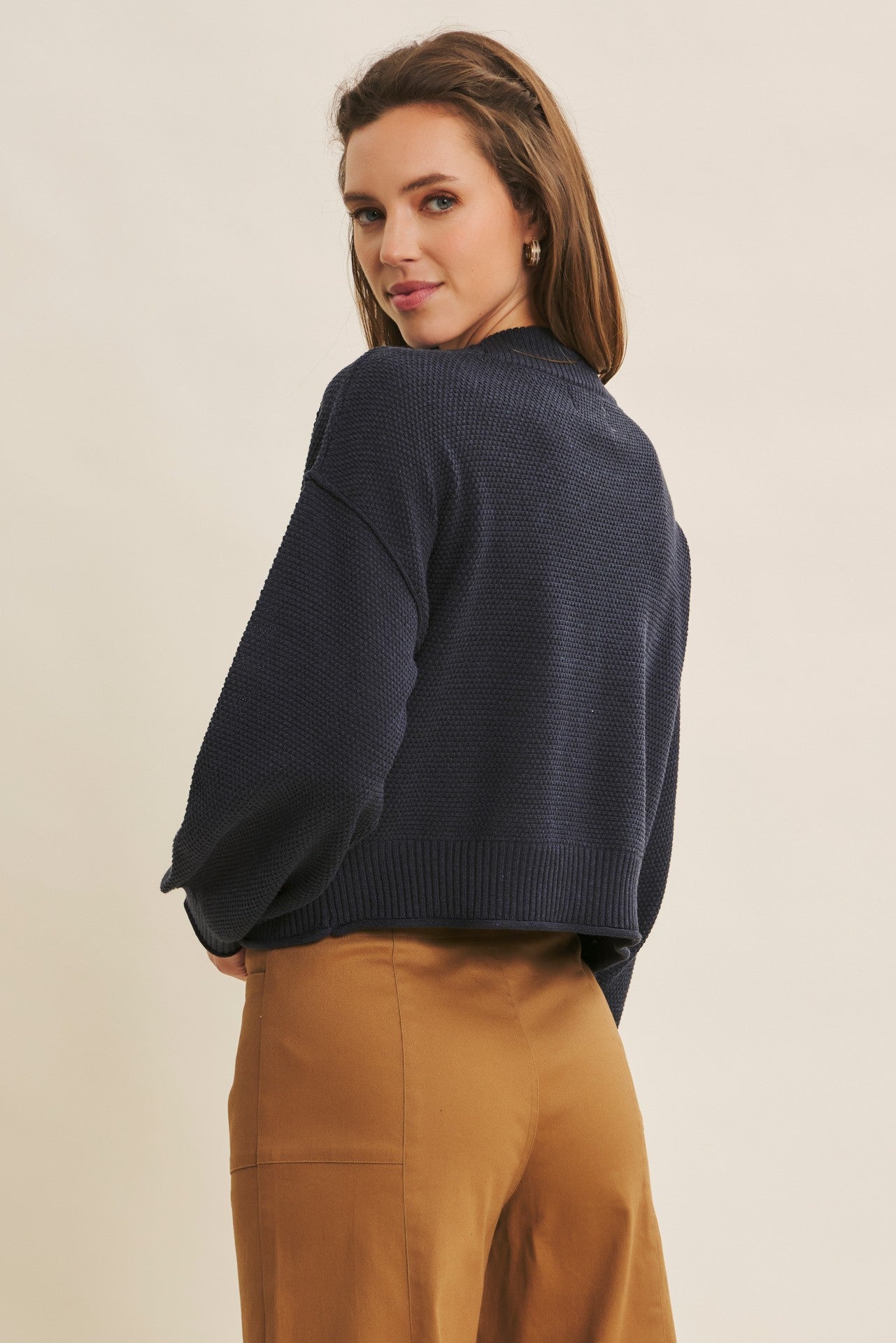 woman wearing a navy cropped sweater with long sleeves and a relaxed fit, paired with tan high-waisted trousers