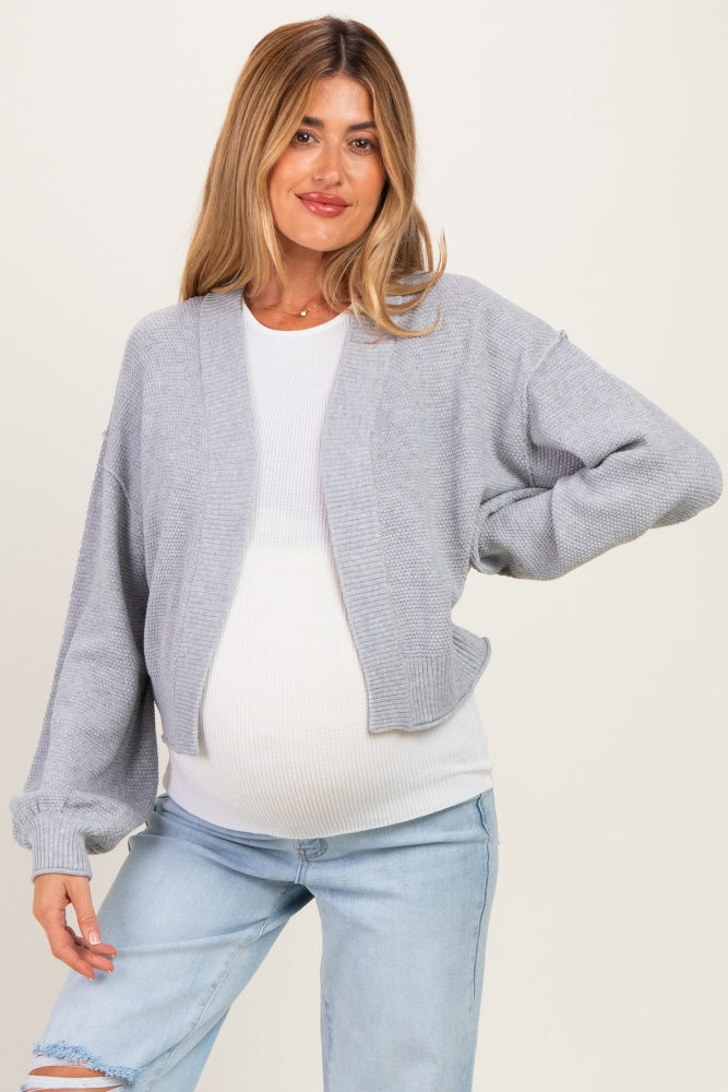 woman wearing a light gray cropped cardigan over a white maternity top and showcasing her baby bump