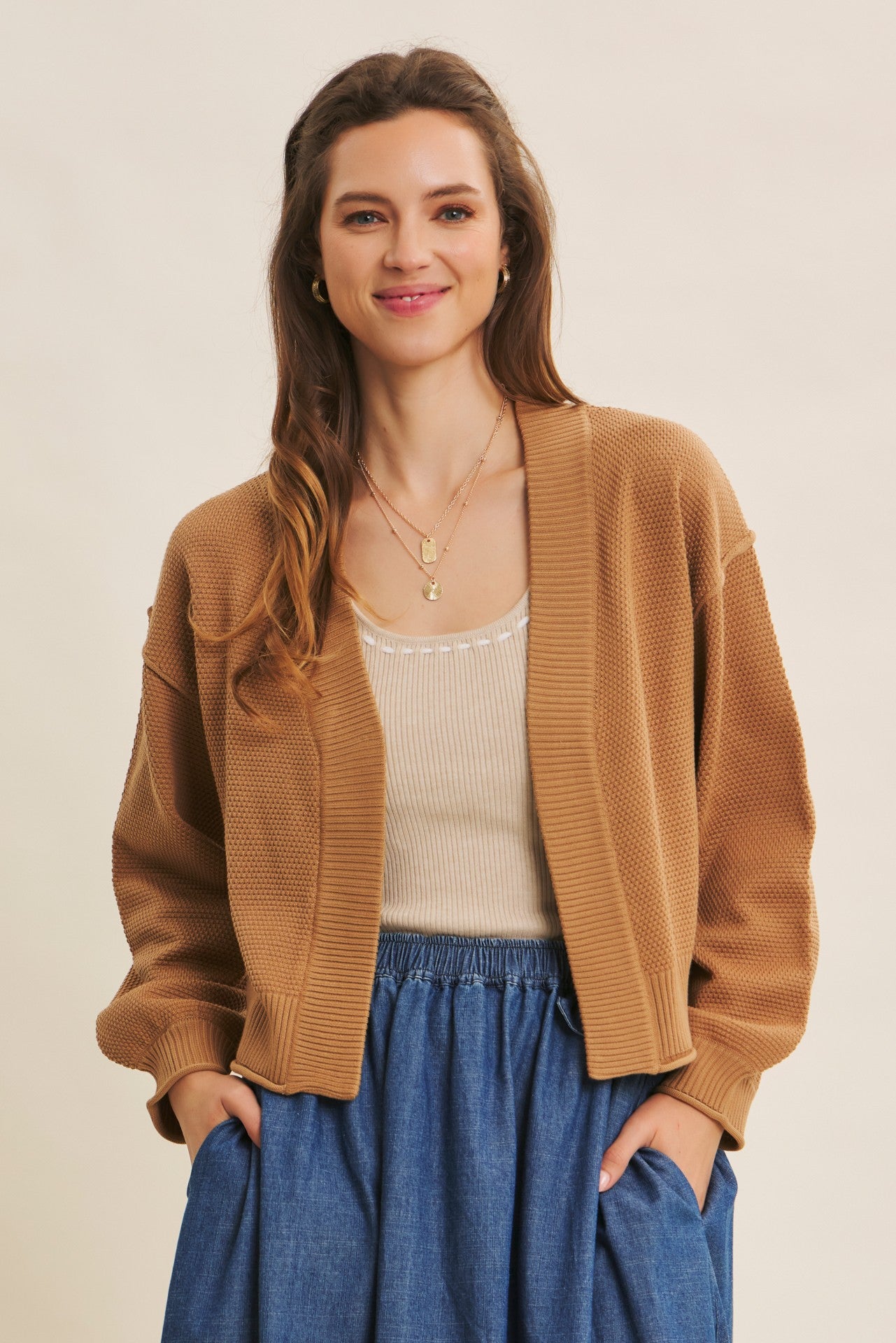 woman wearing a camel-colored cropped cardigan over a cream tank top and paired with a denim skirt
