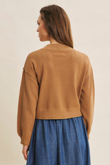 woman wearing a tan cropped sweater over a denim skirt, viewed from the back