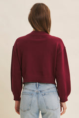 woman wearing a burgundy cropped sweater with balloon sleeves, viewed from the back, paired with light blue jeans