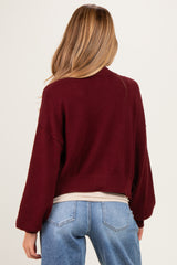 woman wearing a burgundy oversized maternity sweater with balloon sleeves and a cropped hem, showing a relaxed fit
